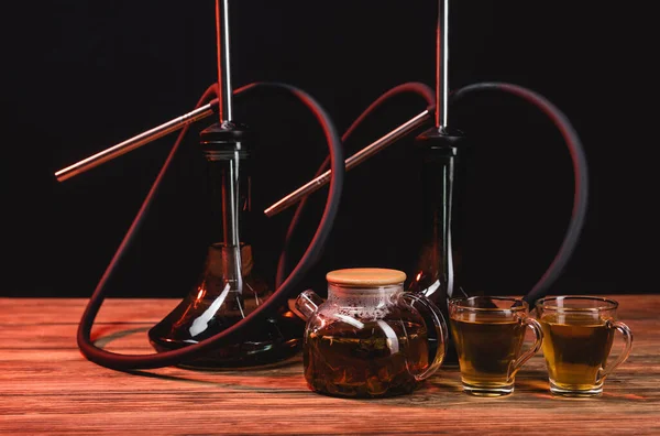 Teapot near hookahs on wooden table isolated on black — Stock Photo