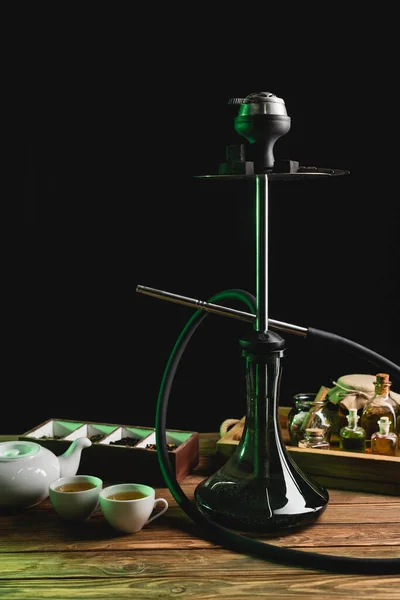 Hookah perto de chá em mesa de madeira isolada em preto — Fotografia de Stock