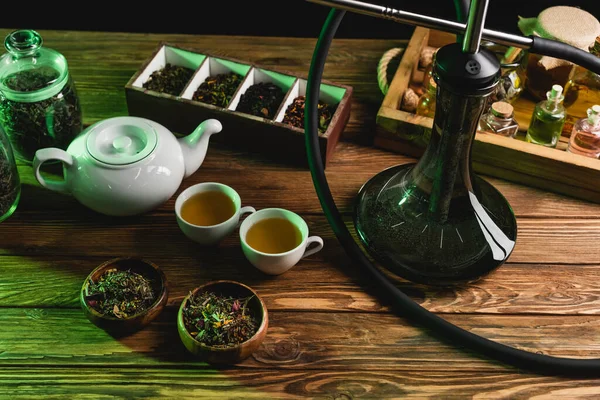 Top view of teapot, dry tea and hookah on wooden surface isolated on black — Stock Photo