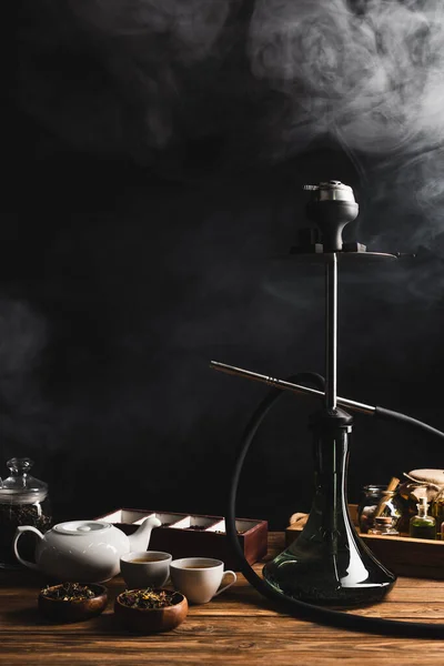 Hookah, tea and teapot on black background with smoke — Stock Photo