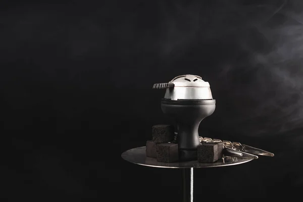 Coals and tweezers on hookah on black background with smoke — Stock Photo