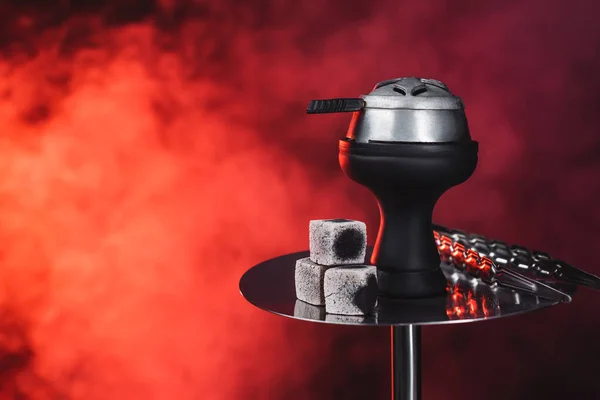 Coals and tweezers on hookah on black background with red smoke — Stock Photo