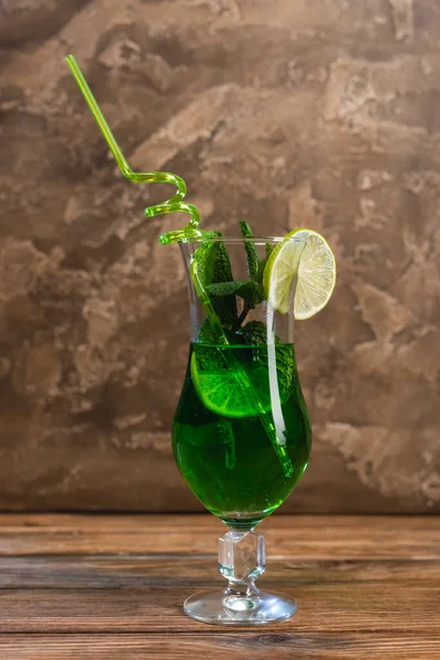Glass of green cocktail with drinking straw on wooden surface on textured stone background — Stock Photo