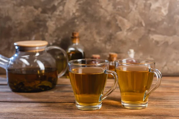 Tazas de té cerca de tetera borrosa en la superficie de madera sobre fondo de piedra texturizada - foto de stock