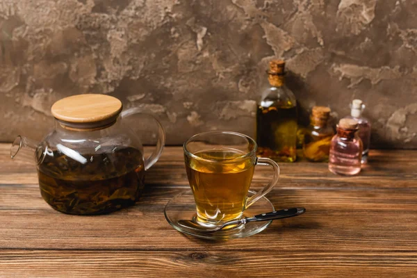 Taza de té cerca de la tetera y botellas borrosas en la superficie de madera sobre fondo de piedra texturizada - foto de stock