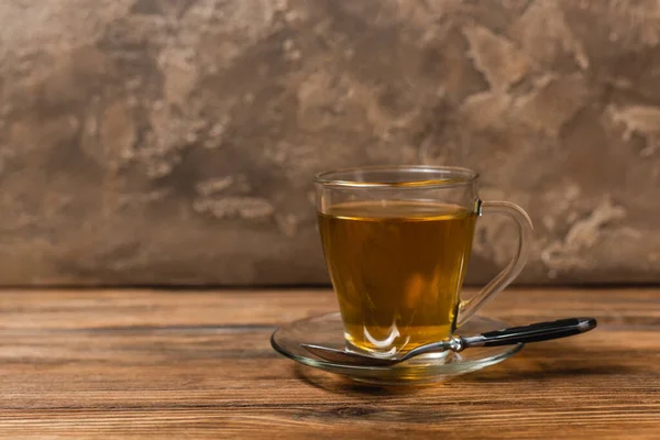 Taza de té en platillo y cuchara en superficie de madera sobre fondo de piedra texturizada - foto de stock