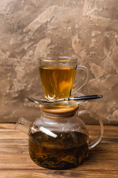 Чашка чаю на скляному чайнику на дерев'яній поверхні на текстурованому кам'яному фоні — стокове фото