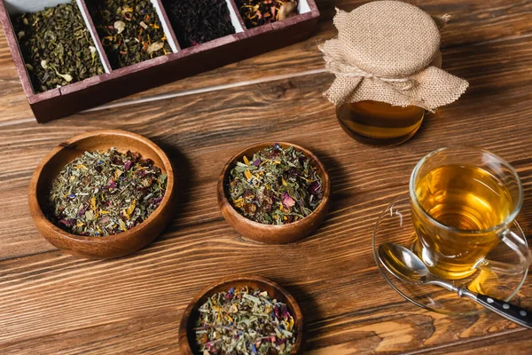 Vista de ángulo alto de té seco en cuencos y tarro con miel en la superficie de madera - foto de stock