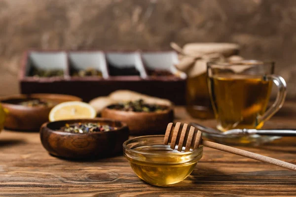 Tigela com mel perto de chá desfocado na superfície de madeira no fundo marrom — Fotografia de Stock