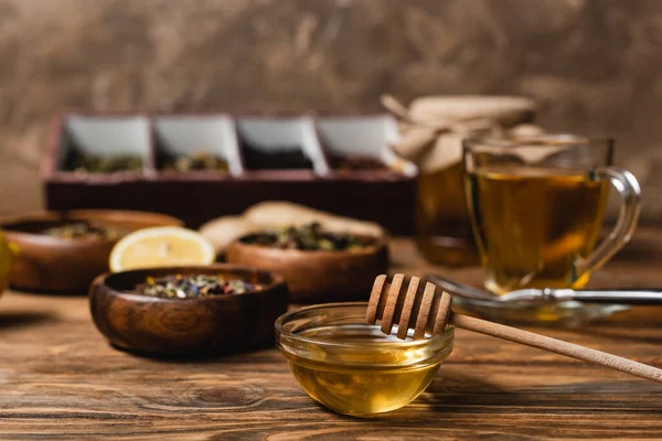 Cuenco con miel cerca de té borroso en la superficie de madera sobre fondo marrón - foto de stock