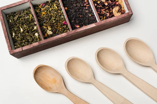 Vista superior de cucharas de madera cerca de té seco en caja sobre fondo blanco - foto de stock