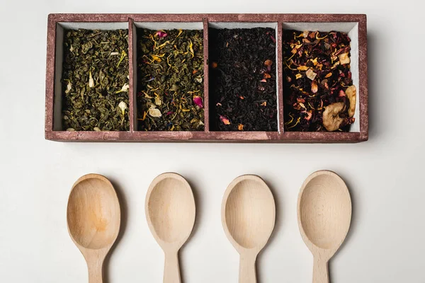 Vista superior del té seco en caja cerca de cucharas de madera sobre fondo blanco — Stock Photo