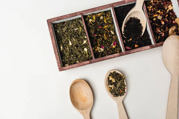 Vista superior de cucharas de madera y té seco en caja sobre fondo blanco - foto de stock