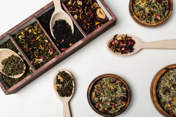 Vue du dessus du thé sec dans une boîte en bois, cuillères et bols sur fond blanc — Photo de stock