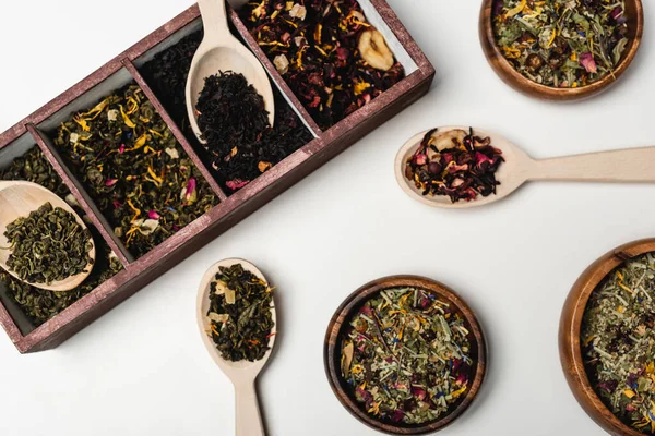 Top view of dry tea in wooden box, spoons and bowls on white background — Stock Photo