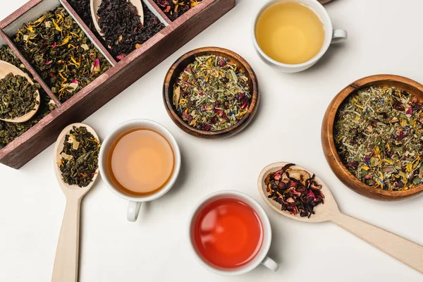 Vista dall'alto di tazze di tè vicino a cucchiai e ciotole di legno su sfondo bianco — Foto stock