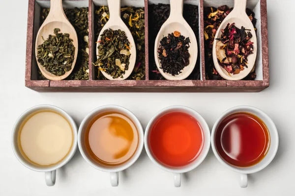 Vue du dessus des tasses de thé près des cuillères en bois et de la boîte sur fond blanc — Photo de stock