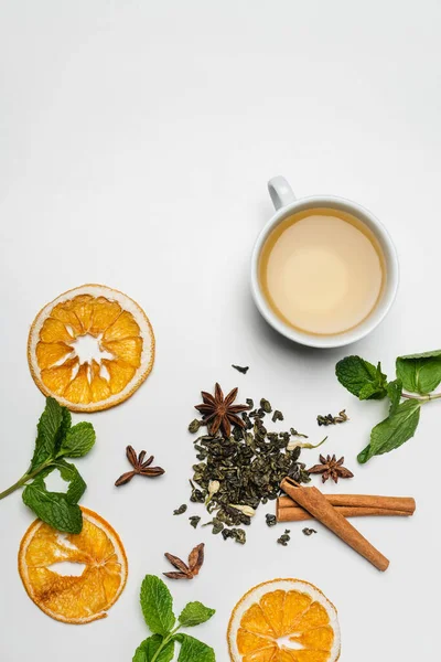 Vue de dessus des tasses de thé près de la menthe, des épices et des tranches d'orange sèches sur fond blanc — Photo de stock