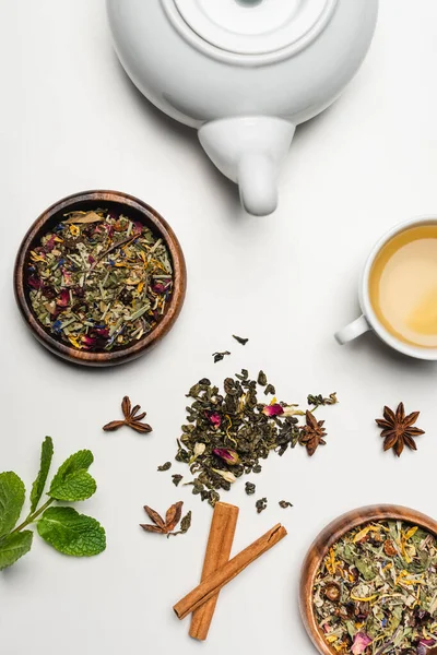 Vue du dessus du thé sec dans des bols, théière et épices sur fond blanc — Photo de stock