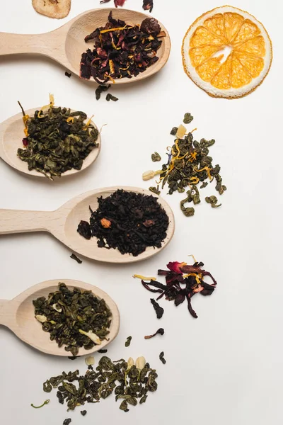 Vista superior del té seco en cucharas cerca de rebanada de naranja sobre fondo blanco - foto de stock