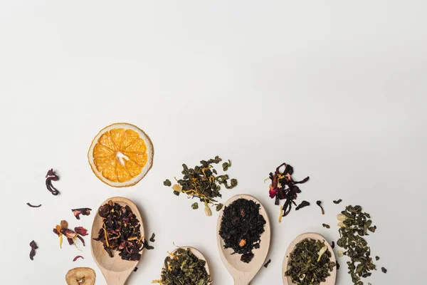 Vista superior del té seco en cucharas de madera cerca de rebanada de naranja sobre fondo blanco — Stock Photo