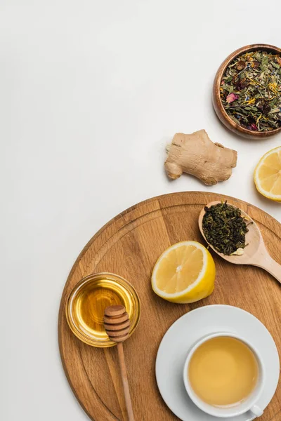 Vista superior de tazas de té, miel y limón sobre tabla de cortar sobre fondo blanco - foto de stock