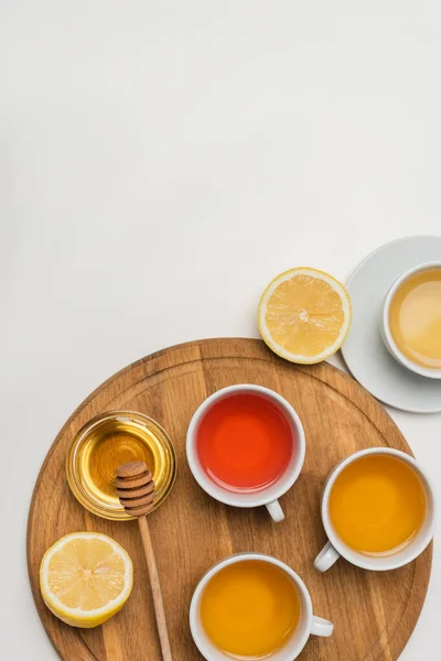 Vista dall'alto di tazze di tè vicino a limone e miele sul tagliere su sfondo bianco — Foto stock