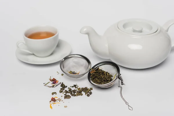 Thé sec en infuseur près de tasse et théière sur fond blanc — Photo de stock
