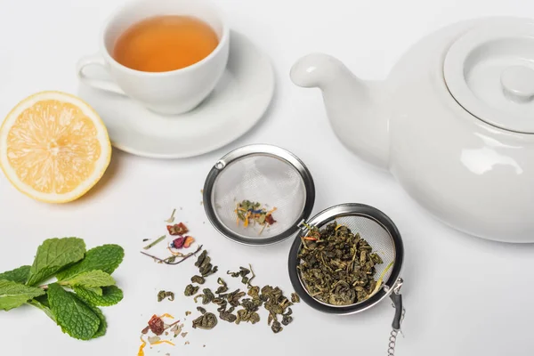 Tè secco in infusore vicino menta, limone e tazza su sfondo bianco — Foto stock