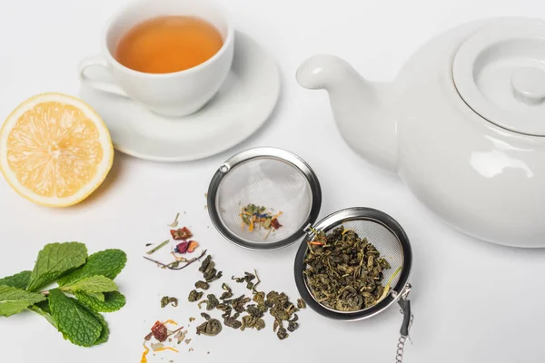 Té seco en infusor cerca de menta, limón y taza sobre fondo blanco - foto de stock