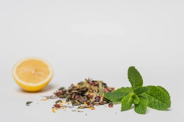 Vista de cerca de la menta cerca del té seco y limón borroso sobre fondo blanco - foto de stock