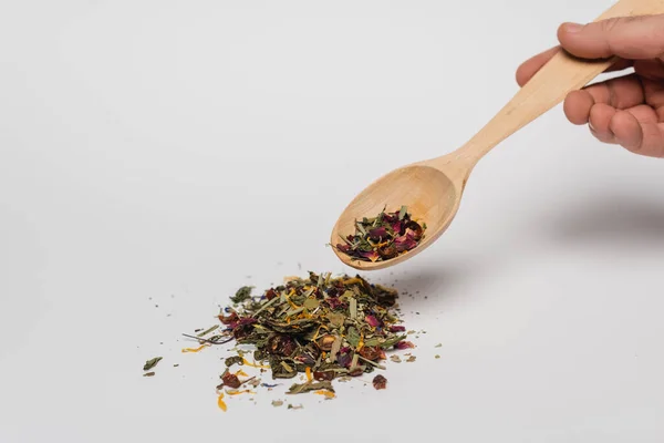 Cropped view of man holding wooden spoon with dry tea on white background — Stock Photo