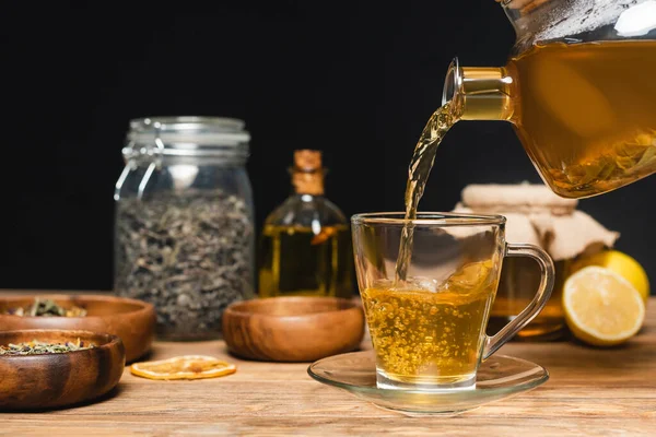 Tetera cerca de la taza, miel borrosa y limones en la superficie de madera aislada en negro - foto de stock