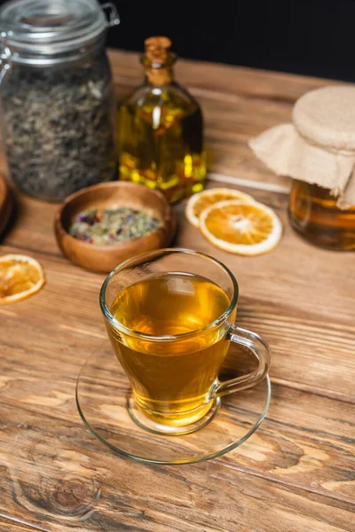 Tasse de thé en verre près de bocaux flous sur la surface en bois isolé sur noir — Photo de stock