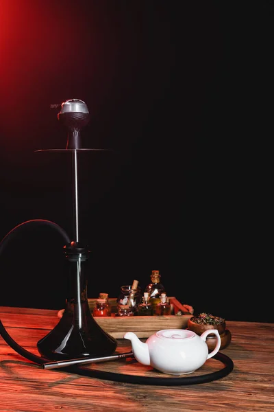 Hookah near teapot and jar on wooden surface on black background — Stock Photo
