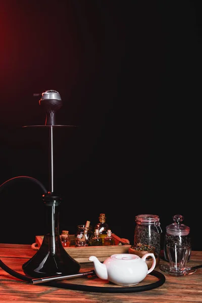 Teapot near jars and hookah on wooden surface on black background — Stock Photo