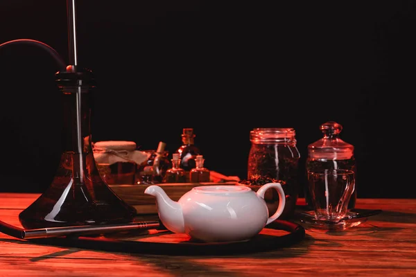 Hookah near teapot and jars on wooden surface isolated on black — Stock Photo