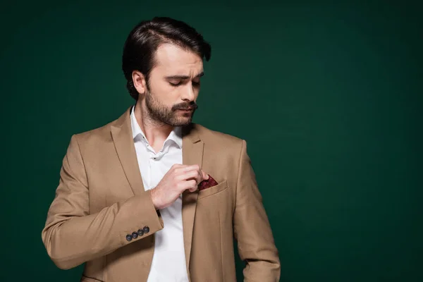 Jeune homme avec moustache ajustant mouchoir dans poche de blazer sur vert foncé — Photo de stock