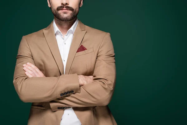 Ausgeschnittene Ansicht eines jungen Mannes mit Schnurrbart, der mit verschränkten Armen auf dunkelgrünem Grund steht — Stockfoto