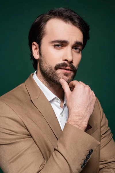 Pensive young man with mustache touching chin on dark green — Stock Photo