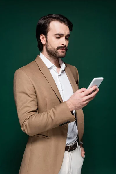 Young man with mustache using smartphone on dark green — Stock Photo