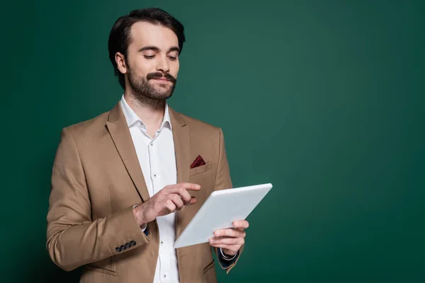 Giovane uomo sorridente con i baffi che tiene tablet digitale su verde scuro — Foto stock