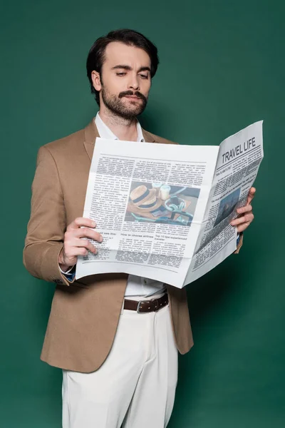 Joven con bigote leyendo periódico de viaje en verde oscuro - foto de stock