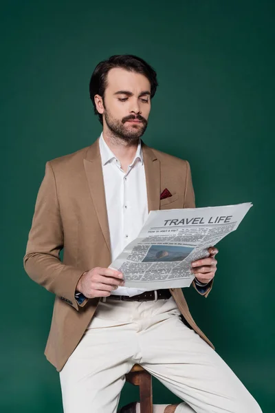 Man with mustache reading travel newspaper on dark green — Stock Photo