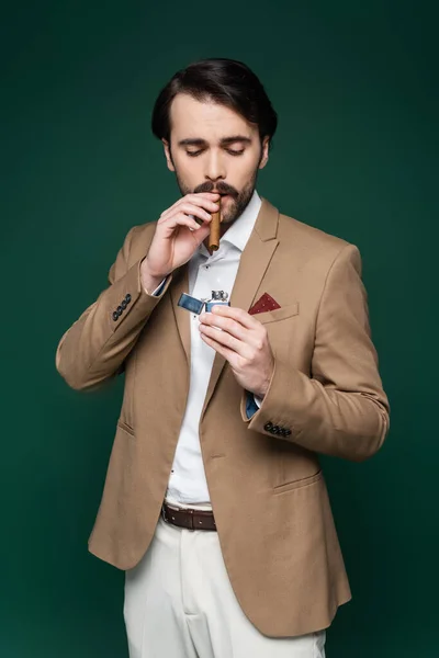 Junger Mann mit Schnurrbart hält Zigarre in der Nähe Feuerzeug auf dunkelgrün — Stockfoto