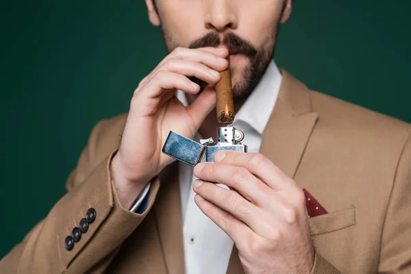 Visão parcial do homem com bigode segurando charuto perto de isqueiro com chama no verde escuro — Fotografia de Stock