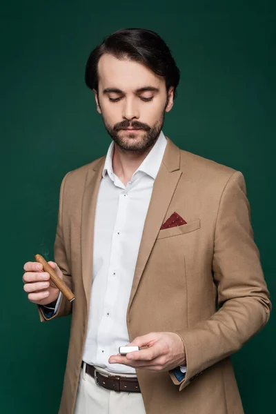 Man with mustache holding cigar and looking at lighter on dark green — Stock Photo