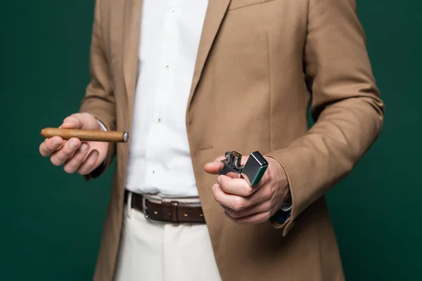 Partial view of man in blazer holding cigar and lighter on dark green — Stock Photo