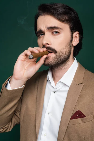 Portrait of man with mustache smoking cigar and looking at camera on dark green — Stock Photo