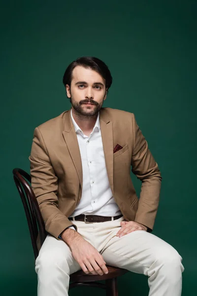 Man in blazer sitting on wooden chair on dark green — Stock Photo